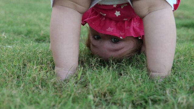 Adorable 1 year baby standing upside down on green grass. 