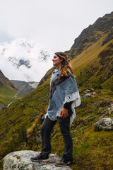 Portrait of a caucasian woman standing, smiling and wearing the typical peruvian poncho on a mountain peak.