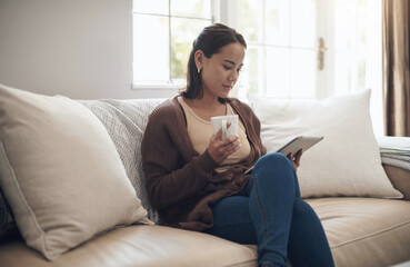 Coffee and a good ebook pairs so well. Shot of a young woman using a digital tablet while drinking coffee at home.