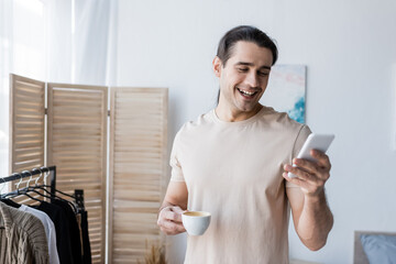 happy man in t-shirt holding cup of coffee and using smartphone.