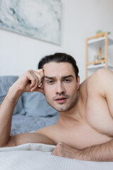 shirtless man resting on bed and looking at camera.