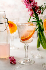 A glass with pink gin cocktail with orange and ice cubes, with pink spring flowers Hyacinth. Alcoholic, refreshing party drink.