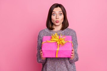 Portrait of attractive amazed girl holding in hands festal gift sending air kiss isolated over pink pastel color background