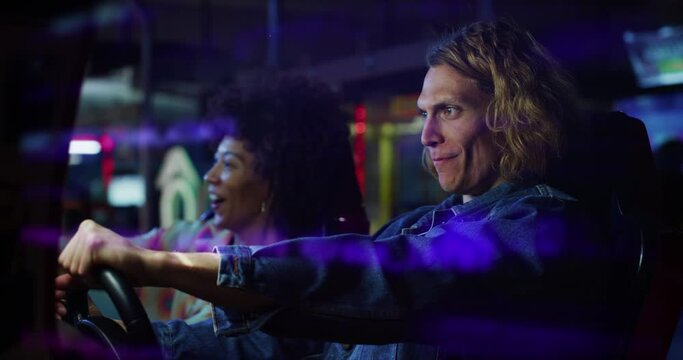 Cinematic shot of young happy interracial couple steering wheel racing in sports car while having fun to play simulation race game together with technologic display in amusement park on weekend.