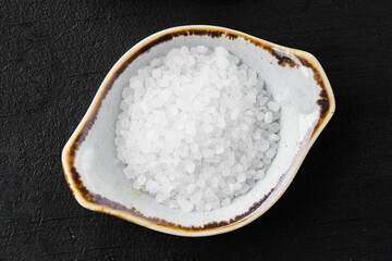 Bowl with salt on black background top view