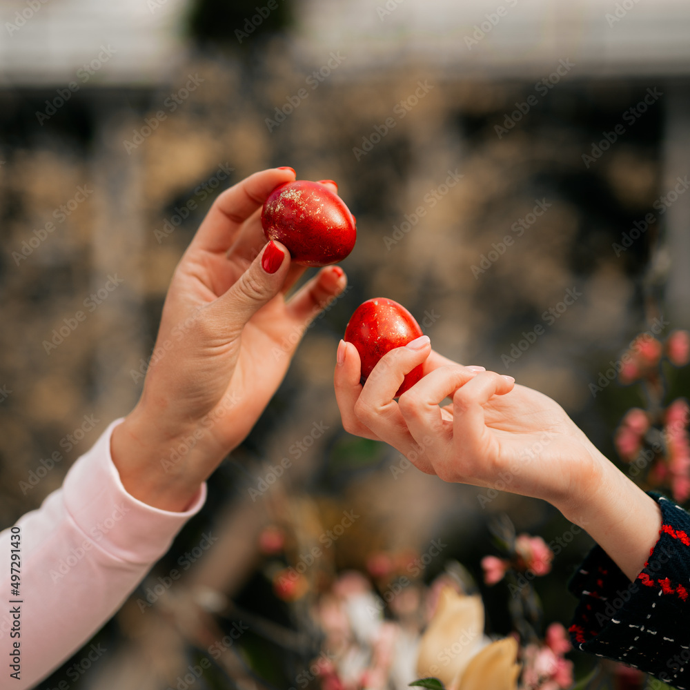 Wall mural two girls have egg tapping with red easter eggs in front off easter table. spring religious traditio