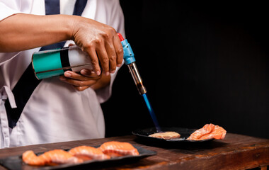 Chef's hand holding fresh piece of salmon.Closeup of chef hands preparing japanese food. Japanese chef making sushi at restaurant.Chef making traditional japanese sushi on wood board.