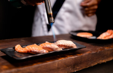 Chef's hand holding fresh piece of salmon.Closeup of chef hands preparing japanese food. Japanese chef making sushi at restaurant.Chef making traditional japanese sushi on wood board.
