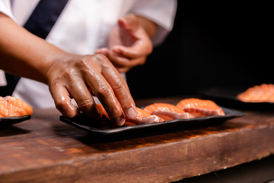 Chef's hand holding fresh piece of salmon.Closeup of chef hands preparing japanese food. Japanese chef making sushi at restaurant.Chef making traditional japanese sushi on wood board.