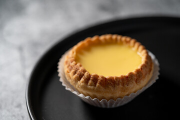 Close up of a piece of fresh Egg Tart on black round plate with cement background
