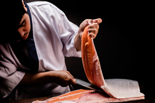 Chef's hand holding fresh piece of salmon.Closeup of chef hands preparing japanese food. Japanese chef making sushi at restaurant.Chef making traditional japanese sushi on wood board.