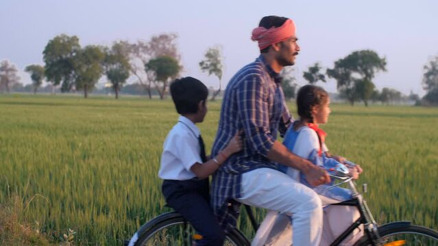 A responsible Indian farmer happily going to drop his little kids to school on a bicycle - village education  Literacy in Rural India. Cheerful siblings of an Indian village crossing an agricultura...