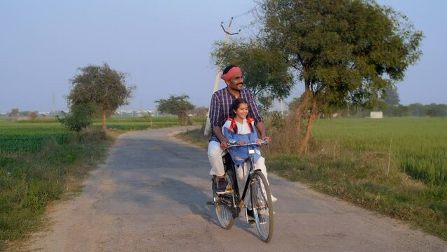 An Indian farmer happily dropping his little daughter to school on a bicycle - Girl-child education  Beti Bachao Beti Padhao. Middle-aged father and his cute daughter while riding home from school ...