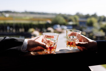 Close up of two hands of men in suits with glasses of whiskey drink outdoors. Alcoholic beverage. High quality photo