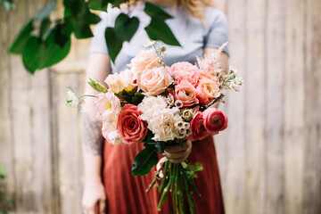 Very nice young woman holding big and beautiful bouquet of fresh roses, chamellacium, eustoma in pink colors, cropped photo, bouquet close up on the wooden background