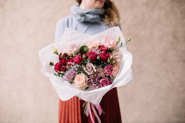 Very nice young woman holding big and beautiful bouquet of fresh roses, carnations, eustoma in pink and burgundy colors, cropped photo, bouquet close up - 497292821