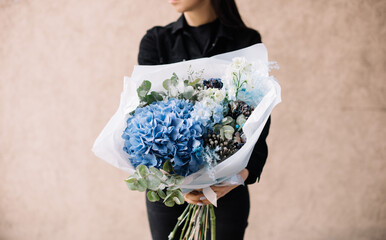 Very nice young woman holding big and beautiful bouquet of fresh hydrangea, delphinium, carnations, eucalyptus, brunia in blue colors, cropped photo, bouquet close up - 497292826
