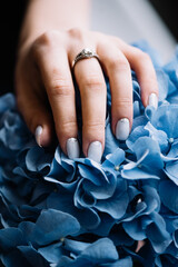 Woman's hand with a beautifully done blue nails holding a blue hydrangea flower, close up vertical...