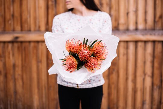 Very nice young woman holding exotic and beautiful mono bouquet of fresh orange nutan proteas , cropped photo, bouquet close up on the wooden background