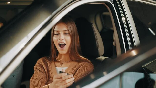 Happy woman taking car key from dealer in auto show or salon. Car dealer giving key to new car owner. Woman receiving car keys from a dealer. Choosing of new vehicle. Concept of expensive purchase