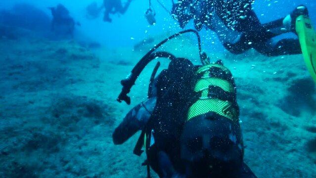 Image of divers swimming under the sea parallel to the cliffs.
