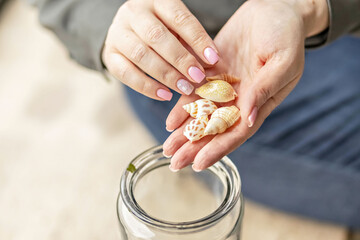 Women's hands hold seashells. Puts the shells in a glass jar. Beach Treasures