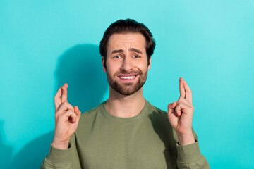 Photo of stressed brunet young guy crossed fingers wear green shirt isolated on teal color...