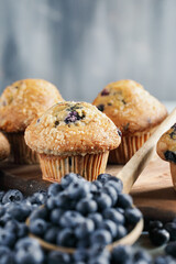 Fresh blueberry muffins with raw blueberries spilling from a wooden spoon in front view. Selective focus on center with blurred foreground and background.