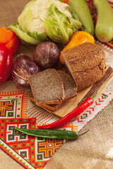 Still life composition of brown whole grain bread with vegetables scattered around. Loaf of organic bread