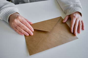 Envelope in hands on a light background. New mail, message. Postal service. The person wants to send or receive a letter. Empty envelope, empty space. The concept of people communication. Mockup 