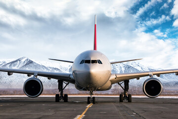 Front view of a wide body passenger aircraft at the airport apron on the background of high picturesque mountains