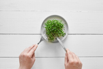 Microgreens arugula sprouts in plate on white table and female hands top view