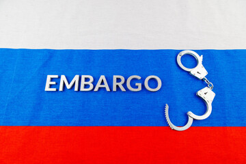 the word embargo laid with silver metal letters on russian tricolor flag with silver handcuffs
