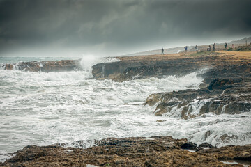 A group of people watching ocean waves against a rocky coast