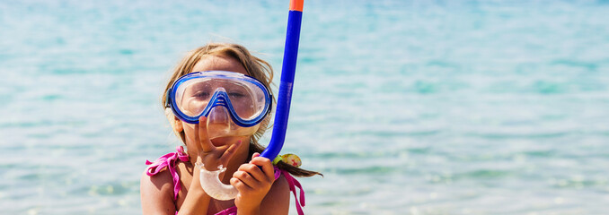 Obraz na płótnie Canvas Funny little girl with mask and snorkel on beach at summer holiday. Summertime fun. Sea water in background. Copy-space.