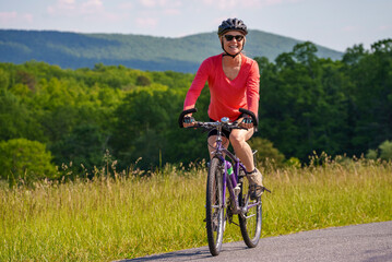 Front view of smiling mature woman biking on a beautiful country road in the mountains on a sunny...