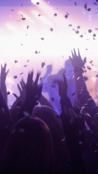 Vertical Footage of Rock Band Performing at a Concert in a Night Club. Front Row Crowd is Partying. Silhouettes of Fans Raise Hands in Front of Bright Colorful Strobing Lights on Stage.
