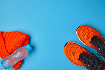 Orange sneakers sports knitted hat and plastic water bottle on a blue background