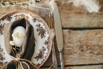 Rustic Easter table setting top view. Natural egg in napkin with flowers, setting  with vintage plate, cutlery, pussy willow branches on aged wooden table. Easter table decoration