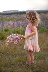 Little pretty cute girl with curly blond hair in summer rose dress in a field of lupines flowers...