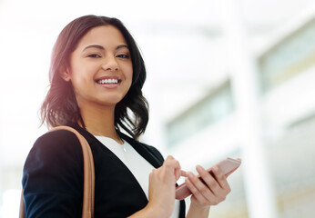 I always make sure Ive got my phone in my hand. Cropped portrait of an attractive young businesswoman smiling while using a smartphone in a modern office.