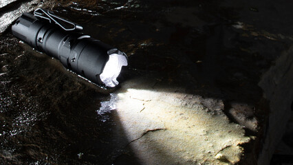 Watertight flashlight on a wet rock - obrazy, fototapety, plakaty
