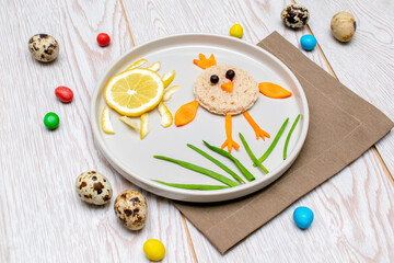 Easter funny creative healthy breakfast lunch food idea for kids, children. chicken shape sandwich from bread, peeled carrots, greens vegetables on plate wooden table background. Top view Flat lay