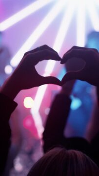 Vertical Format Video of a Person Making a Heart Sign Gesture and Holding Hands Up at a Performance. Rock Band Playing a Song at a Concert in a Night Club on Stage.