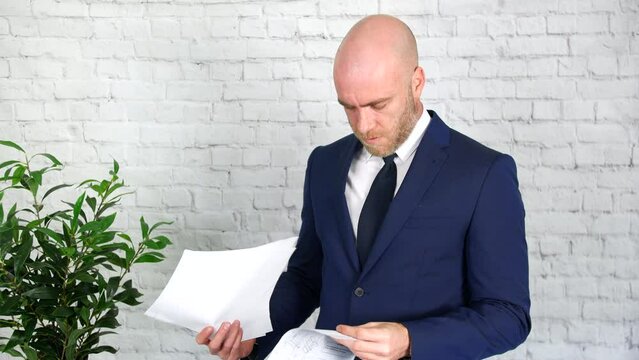 A businessman is upset after reading through papers which he then throws in the air. He looks angry and stressed.
