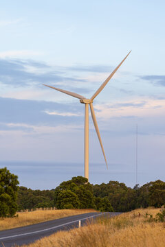 Looking along a road going over a rise to a tall wind turbine against a pastel sky