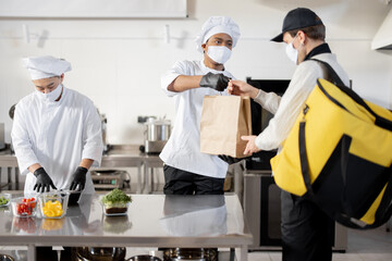 Courier waiting for an order for delivery in the kitchen with chefs preparing takeaway food....