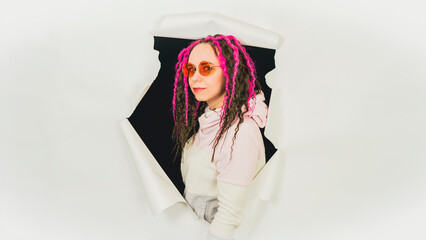 Stylish woman in trendy outfit and sunglasses. Confident young female in trendy outfit and sunglasses looking at camera while standing in hole of white background.