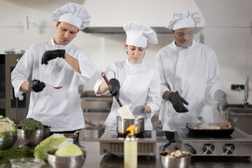 Multiracial team of three cooks in uniform cooking together in the professional kitchen. Latin cook...