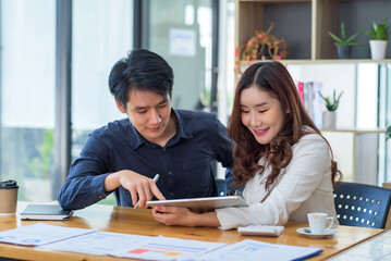 Young Asian businesswoman and businessman discuss investment project working and planning strategy on digital tablet. Business people talking together with tablet at office.